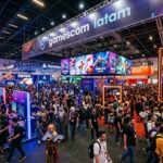 Vista panoramica de um salao de convencao de jogos em Sao Paulo, lotado de visitantes, com luzes de telas e uma atmosfera vibrante de evento de games.