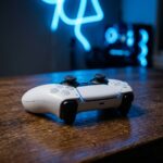 Controle de PS5 DualSense sobre uma mesa de madeira escura com iluminacao suave azul de neon ao fundo, estilo fotografia editorial.